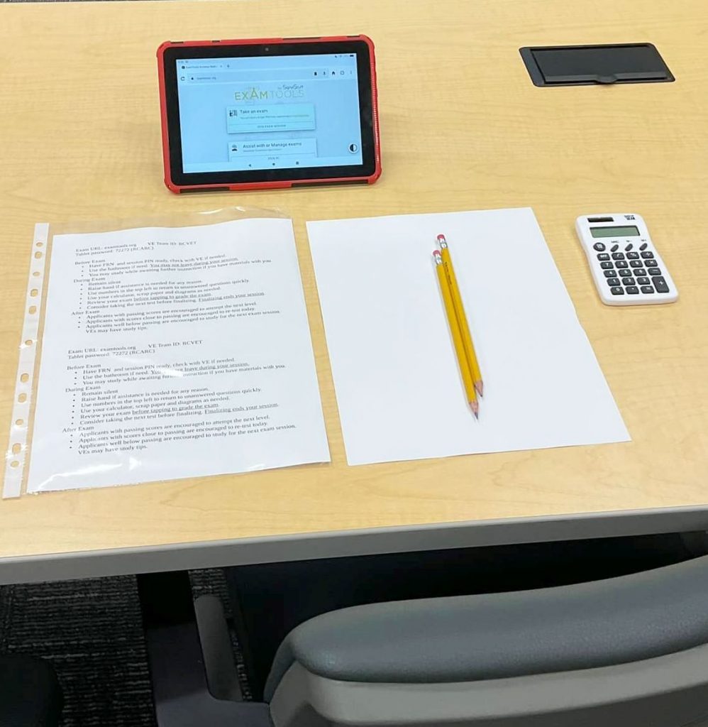 Examination participant station with a tablet, printed instructions, calculator, pencil and scrap paper.