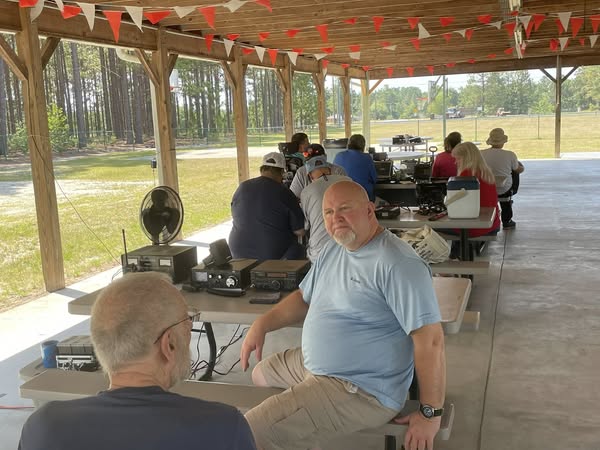Field day at the pick-nick table under the pavilion, James Bullard at his station talking with another member.