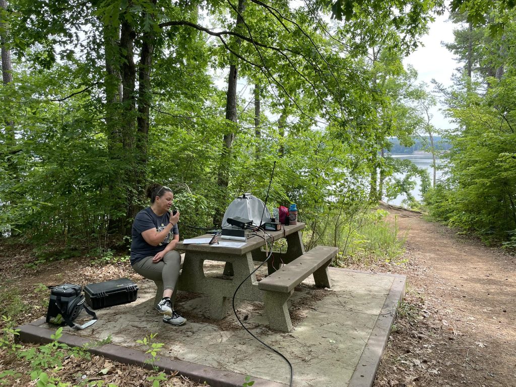 Olivia Rinehart at the pick-nick table in the woods with her radio gear, activating a park for Parks On The Air (POTA)